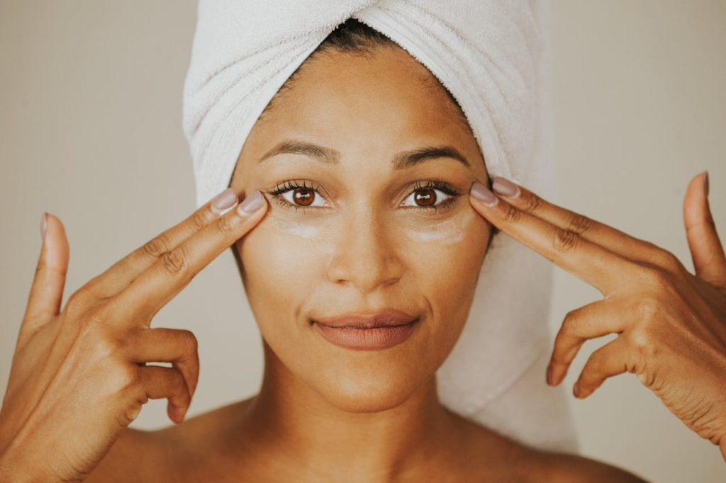 Woman applying facial cream with a towel wrapped on her head, highlighting skincare routine.